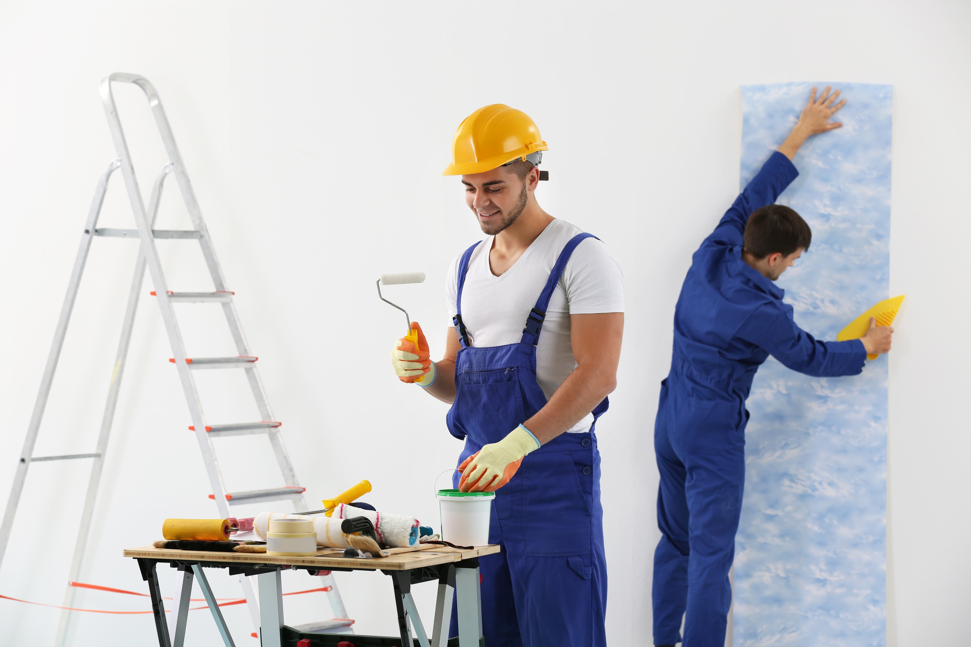 Two workers in hard hats painting and installing wallpaper for home installation services at Aurora Home Hardware Building Centre.