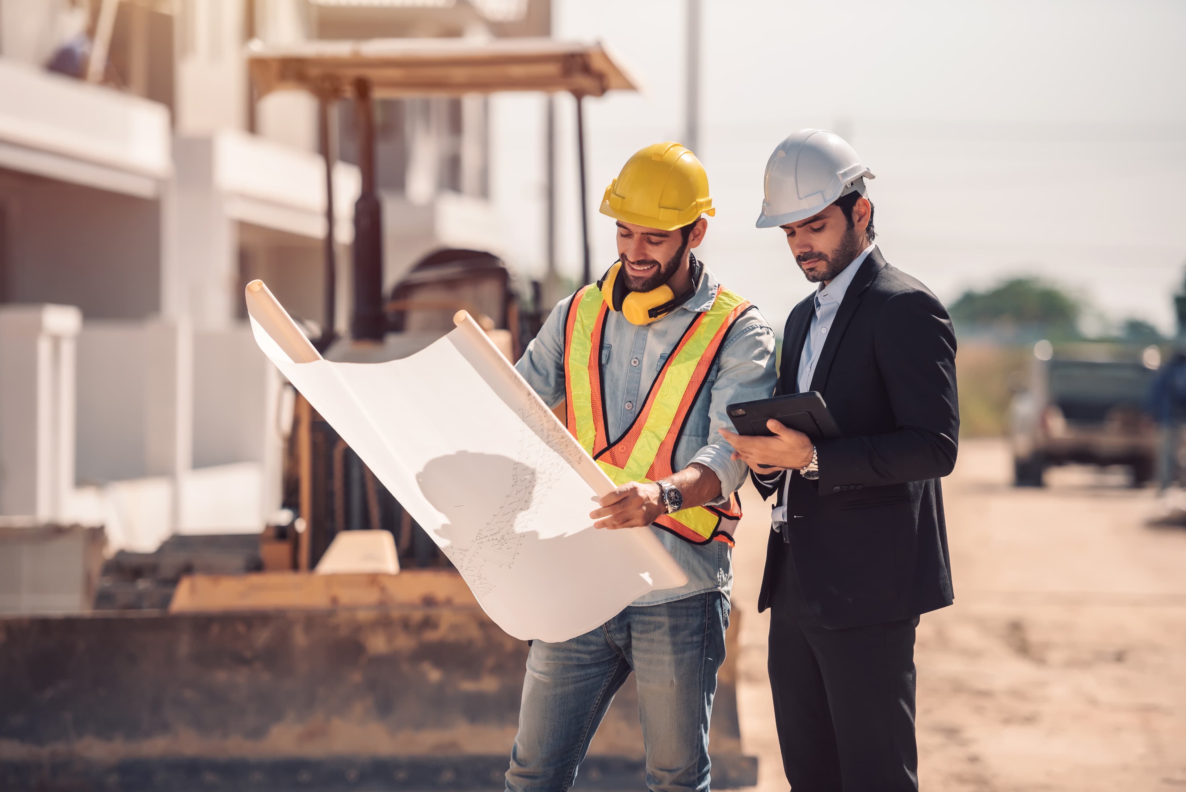 Two contractors reviewing blueprints on a job site accessing Aurora Home Hardware Building Centre PRO Contractor Services through a tablet.