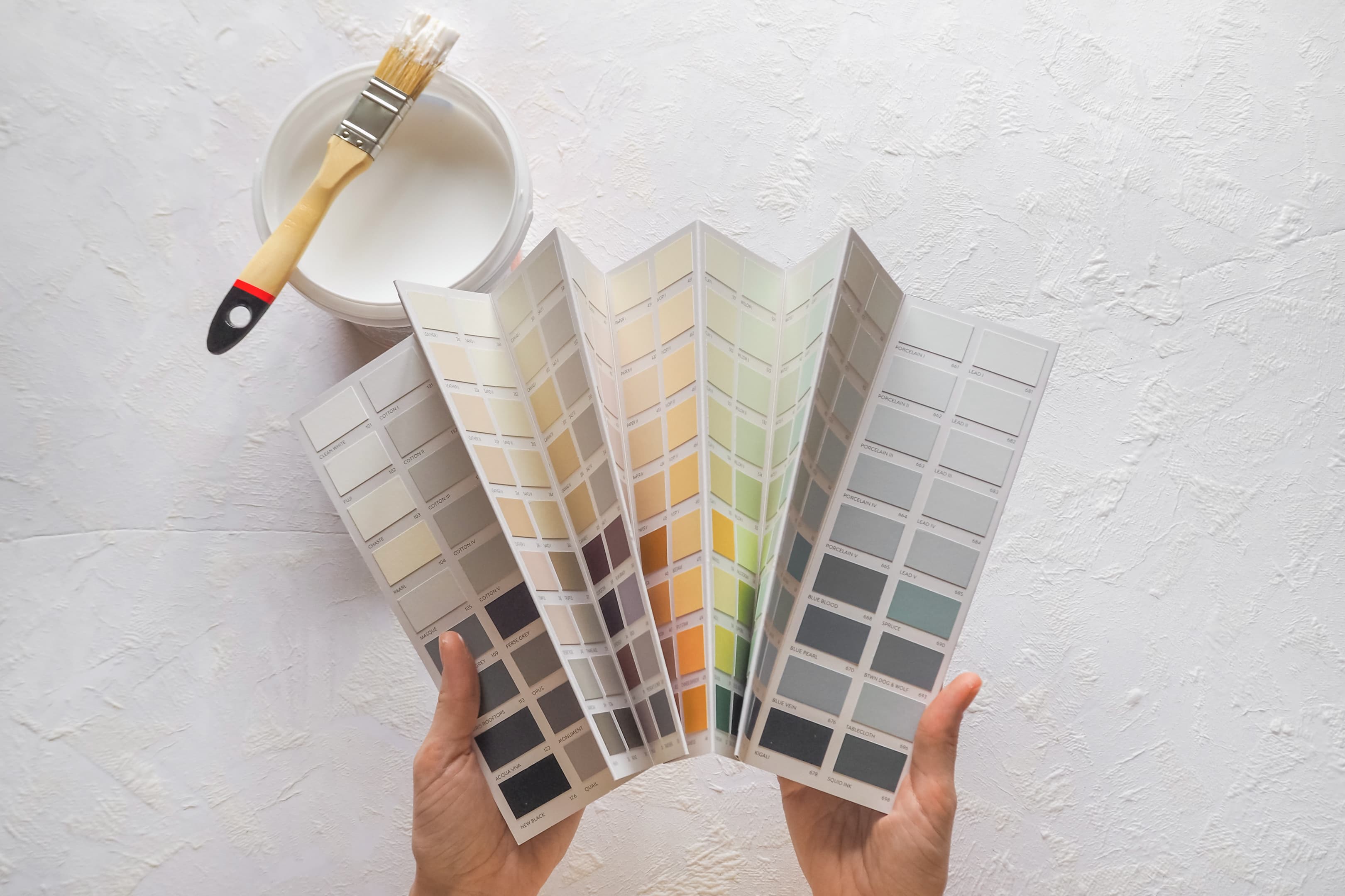 A hand holding paint colour swatch fans with a brush and paint can for paint mixing and colour matching at Aurora Home Hardware Building Centre.